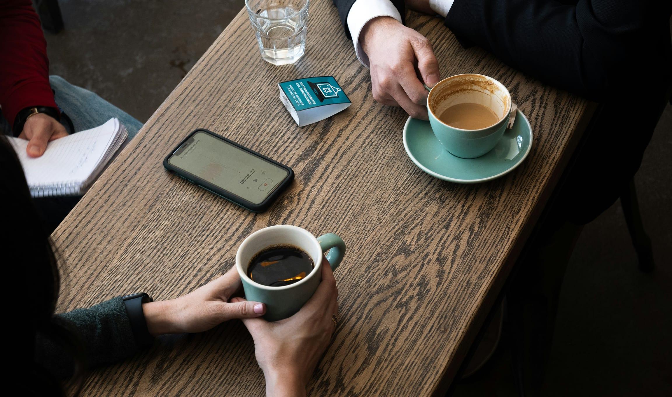 Deux personnes autour d’un café, un carnet et un téléphone sur une table en bois