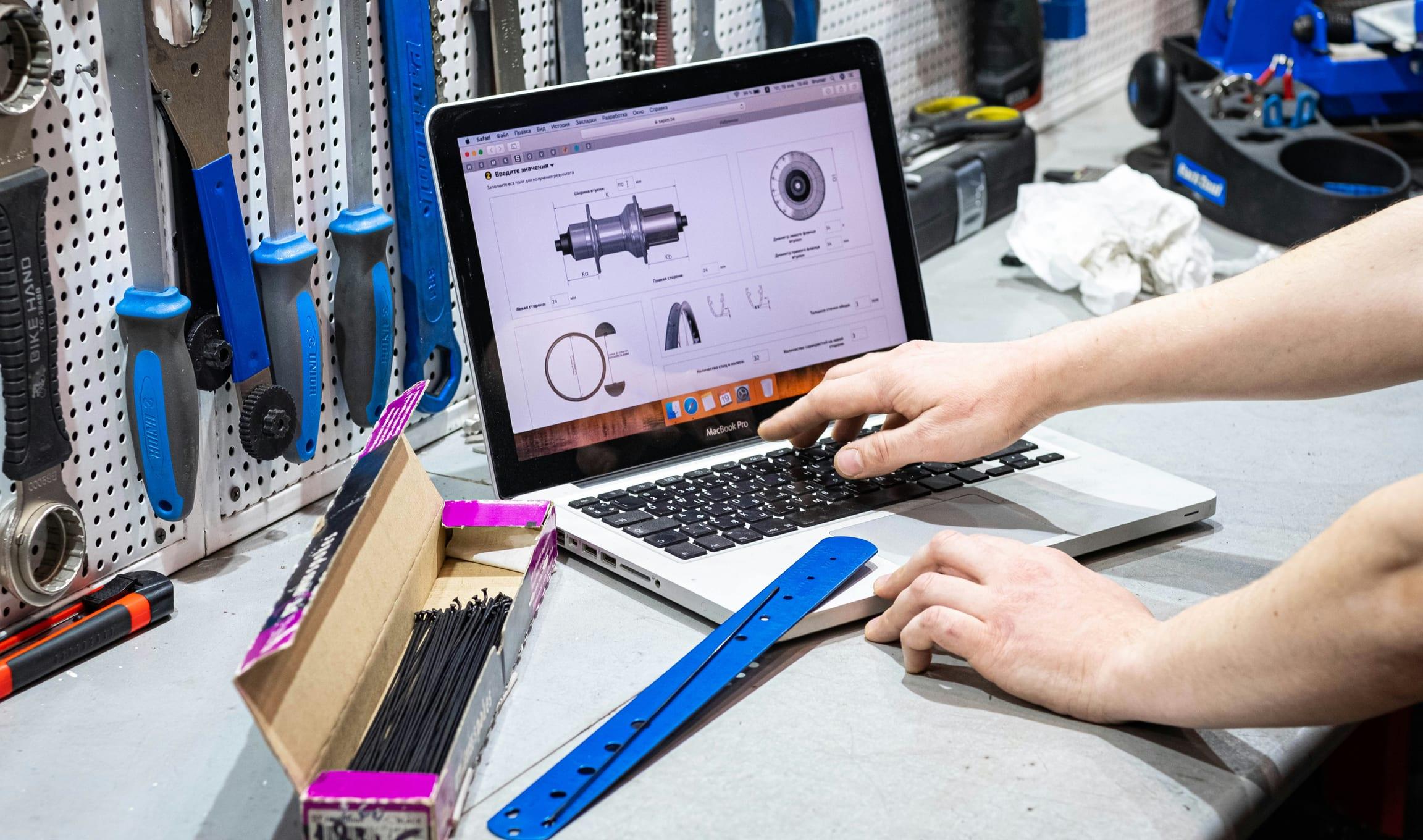 Mains sur un ordinateur portable dans un atelier, outils accrochés au mur