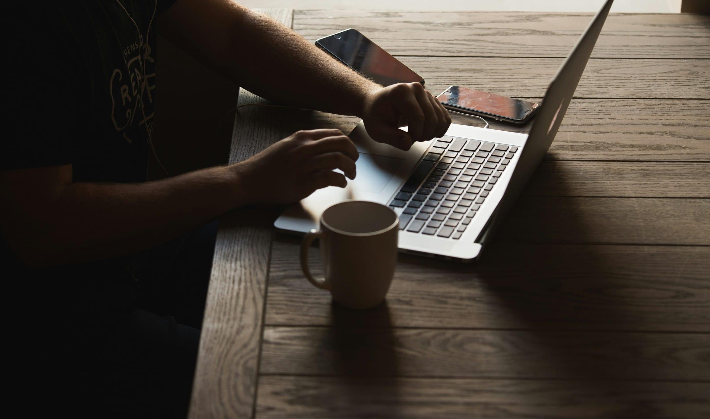 Mains sur un ordinateur portable, téléphones et tasse sur une table en bois